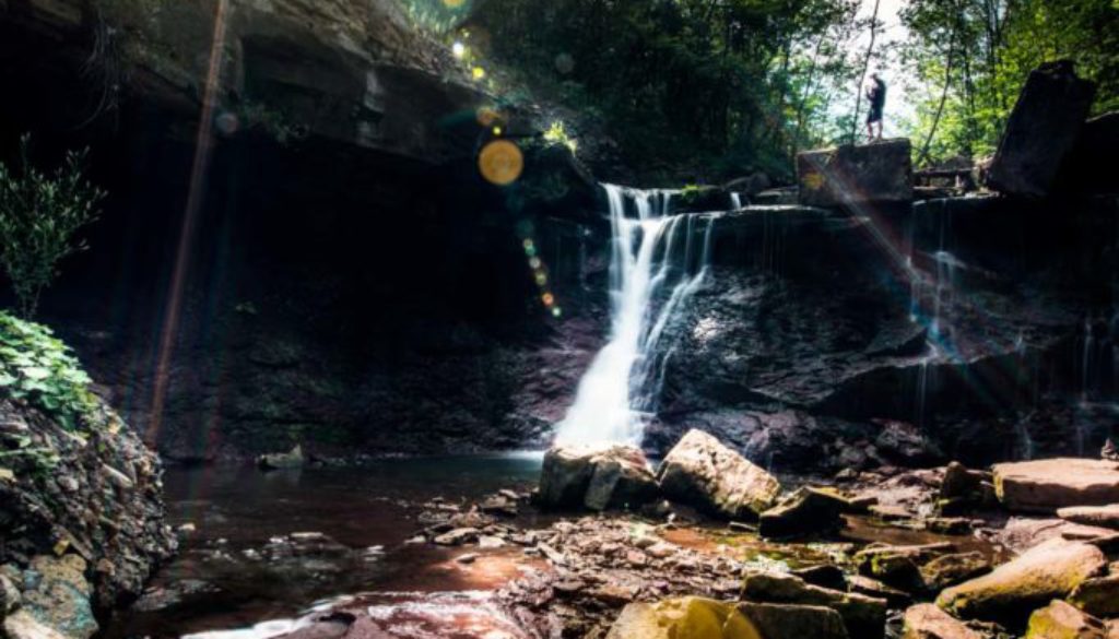 image of man standing at the top of chedoke waterfall in hamilton ontario with sunrays beaming through