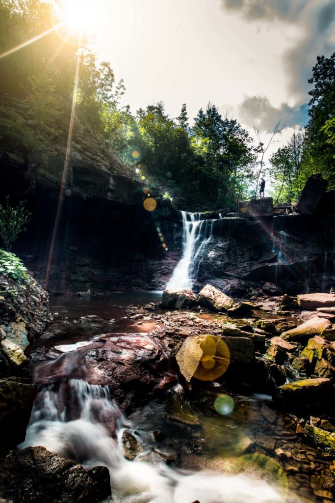 image of man standing at the top of chedoke waterfall in hamilton ontario with sunrays beaming through